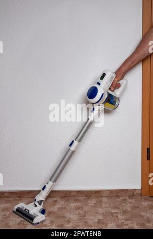 Person, die saugt. Der Mann reinigt den Teppich im Zimmer mit einem Akku-Staubsauger. Hausarbeit. Hoover in Aktion. Stockfoto