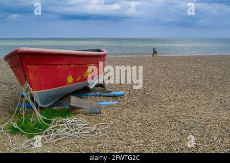 Rotes Fischerboot und eingeflügelter Fischer am Strand Stockfoto