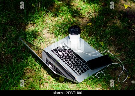 Laptop mit Mobiltelefon-Headset und Kaffee auf grünem Gras. Agiles Geschäft. Online-Studie. Sommerstimmung. Entspannen. universitätsstudenten leben Stockfoto