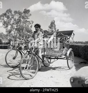In den 1950er Jahren, indisches Fahrradtaxi, mit Fahrern, die auf Kunden warteten, Indien, waren diese Fahrradfahrracks ein kleiner Nahverkehr, eine Art Dreirad mit Heckklappe, und sie würden Passagiere auf Mietbasis transportieren und unter verschiedenen Namen bekannt sein: Fahrradtaxi, Velo-Taxi, Trishaw oder Heckfahrrad. Cycle Rikschas entstanden in den 1880er Jahren in Asien. In den späten 1920er Jahren waren sie in Singapur weit verbreitet und bis 1950 überall in Süd- und Ostindien zu finden. Es gibt verschiedene Designs, in Indien sitzen die Passagiere hinter dem Fahrer. Stockfoto