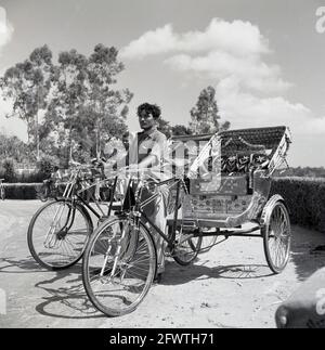 In den 1950er Jahren, indisches Fahrradtaxi, mit Fahrern, die auf Kunden warteten, Indien, waren diese Fahrradfahrracks ein kleiner Nahverkehr, eine Art Dreirad mit Heckklappe, und sie würden Passagiere auf Mietbasis transportieren und unter verschiedenen Namen bekannt sein: Fahrradtaxi, Velo-Taxi, Trishaw oder Heckfahrrad. Cycle Rikschas entstanden in den 1880er Jahren in Asien. In den späten 1920er Jahren waren sie in Singapur weit verbreitet und bis 1950 überall in Süd- und Ostindien zu finden. Es gibt verschiedene Designs, in Indien sitzen die Passagiere hinter dem Fahrer. Stockfoto