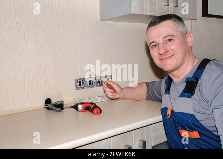 Ein Elektriker installiert Steckdosen in der Küche. Werkzeuge in der Hand. Modernes Design Stockfoto