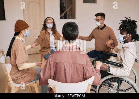 Verschiedene Gruppen von Menschen, die während der Therapiestunde die Hände im Unterstützungskreis halten, alle mit Masken Stockfoto