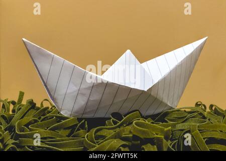 Ein Papierboot auf einer grünen Falle wie das Meer Stockfoto