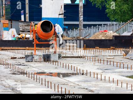 Ein großer orangefarbener Mörtelmischer steht vor dem Hintergrund eines Arbeitsbereichs zur Reparatur von Fugen auf einer Betonstraßenoberfläche. Selektiver Fokus, Kopierbereich. Stockfoto