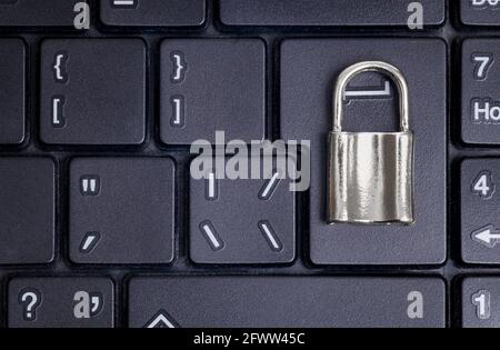 Nahaufnahme eines kleinen verschlossenen Vorhängeschlosses auf einer schwarzen Laptop-Tastatur. Datenschutzkonzept. Stockfoto