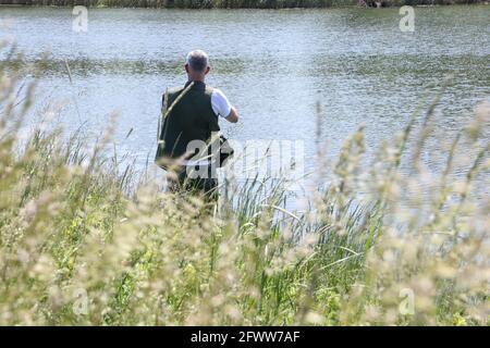 Rückansicht EINES Fischers durch das schwankende Gras. Immer weg von allem und gehen in die Natur gehen zum Angeln. Stockfoto