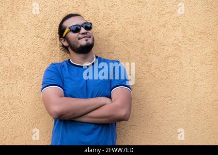 Porträt eines jungen Latinos und bärtigen Mannes, der auf gelbem Hintergrund mit gekreuzten Armen und Brille steht. Horizontal angeschossene Frischluft Stockfoto
