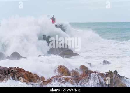 Rote Struktur des Leuchtfeuers auf North Rock im Meer gehüllt Und sprühen Sie die Basis des Mount Maunganui mit wilden Dramatik Stürmische See, die um und über sie krachen Stockfoto