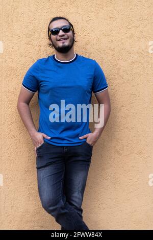 Junger Latino-Mann mit Sonnenbrille und Händen in den Taschen lächelnd und Blick auf die Kamera. Vertikale Aufnahme. Frisches Konzept Stockfoto