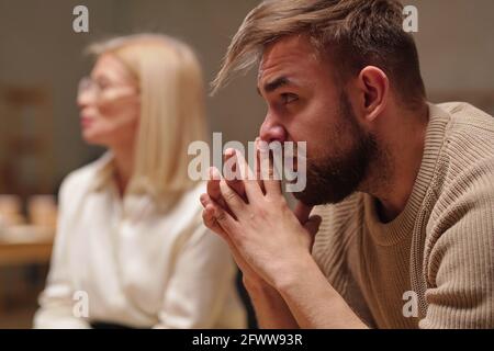 Nachdenklicher junger Mann, der beim Zuhören Hände an Gesicht hält Jemand Stockfoto
