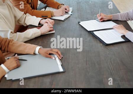 Nahaufnahme eines nicht erkennbaren Kandidaten, der am Tisch sitzt und das Dokument unterzeichnet Während der Annahme eines Stellenangebots nach einem Gespräch mit Personalvermittlern Stockfoto