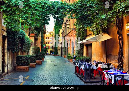 Schöne alte Straße in Rom gesäumt mit grünen Weinstöcken und Cafétischen, Italien Stockfoto