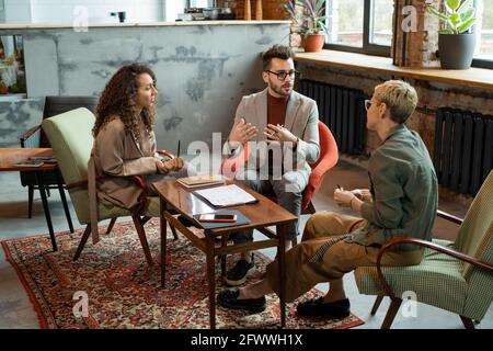 Drei junge Designer diskutieren bei Treffen im modernen Büro Stockfoto