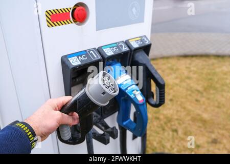 Elektrische Tankstelle für Elektrofahrzeuge. Der Mann nimmt den Kontaktdraht, um die Maschine anzuschließen Stockfoto