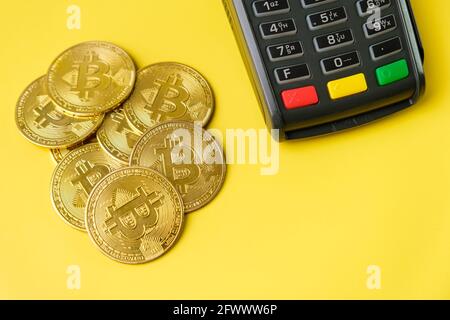 Bitcoin-Münzen in der Nähe des POS-Zahlungsterminals auf dem gelben Hintergrund. Krypto-Währung für die Zahlung Stockfoto