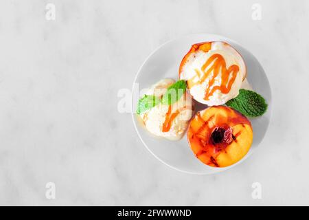 Köstliche gegrillte Pfirsiche mit Vanilleeis und Karamellsoße. Blick von oben auf weißem Marmor. Stockfoto