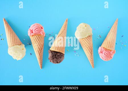 Eiskonus flach auf blauem Hintergrund. Aromen von weißer Vanille, rosa Erdbeere und dunkler Schokolade. Stockfoto