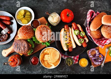 Sommer BBQ Food Tisch mit Hot Dog und Hamburger Buffet. Draufsicht über einen dunklen Schieferhintergrund. Stockfoto