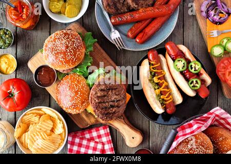 Sommer BBQ Food Tischszene mit Hot Dog und Hamburger Buffet. Draufsicht über einen dunklen Holzhintergrund. Stockfoto