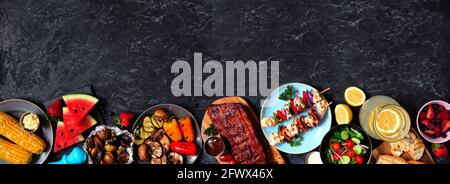 BBQ oder Picknick-Essen im Sommer Grenzen über einem dunklen Stein Banner Hintergrund. Verschiedene Grillgerichte, Gemüse, Obst, Salat und Kartoffeln. Overhead-Ansicht wi Stockfoto