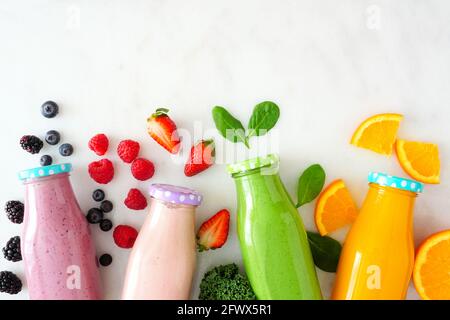 Sortierte gesunde Frucht-Smoothies in Flaschen mit Zutaten. Blick von oben auf weißem Marmor. Heidelbeere, Erdbeere, Grün und Orange. Stockfoto