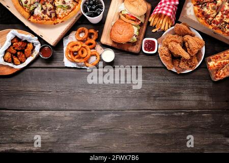 Verschiedene Gerichte zum Mitnehmen und Fast Food. Pizza, Hamburger, gebratenes Huhn und Beilagen. Oberer Rand. Oben auf einem dunklen Holzhintergrund mit Kopierraum. Stockfoto