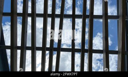 Ein graues Pergola-Dach aus Holz in einem Park mit hellblauem Himmel und weißen, flauschigen Wolken. Stockfoto