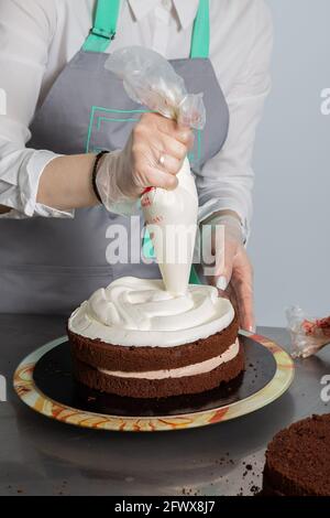 Frau überreicht dem Koch die Creme auf der zweiten Schicht des Schokoladenkuchens. Schokoladenkuchen. Serie. Stockfoto