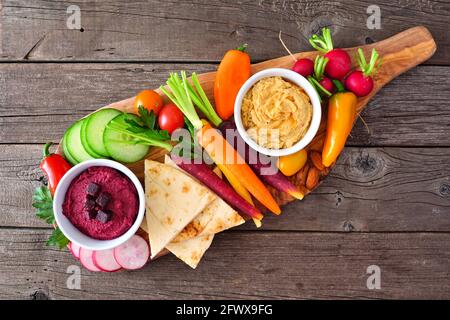 Auswahl an frischem Gemüse und Hummus Dip auf einem Servierbrett. Blick von oben auf einem rustikalen Holzhintergrund.