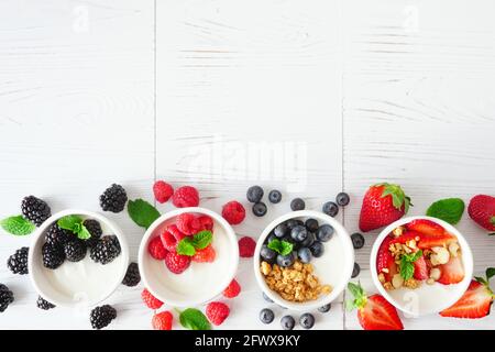 Gesunde Joghurtschüsseln mit verschiedenen Beeren und Müsli. Unterer Rand vor einem weißen Holzhintergrund. Speicherplatz kopieren. Stockfoto
