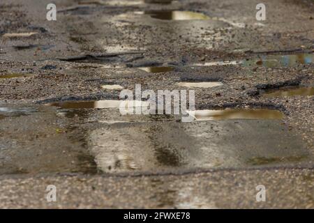 Schlaglöcher und Pfützen auf schlecht gebrochener nasser Asphaltstraße danach Rain – Vollformathintergrund Stockfoto