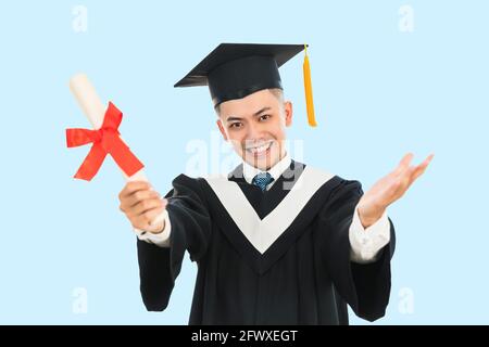 Aufgeregt junger Mann in schwarzem Abschlusskleid und Mütze halten Ein Diplom Stockfoto