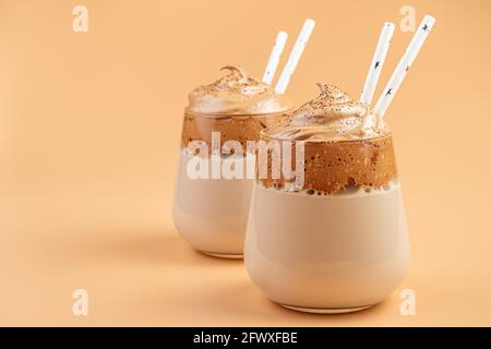 Dalgona-Kaffee-Nahaufnahme in zwei klaren Gläsern mit Trinkhalmen auf orangefarbenem Hintergrund. Stockfoto