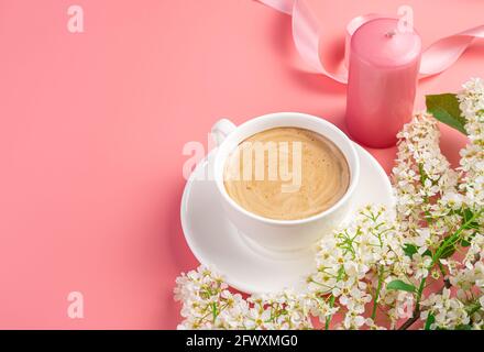 Kaffee in einer weißen Tasse, Kerze und Blumen auf einem rosa Hintergrund mit Platz zum Kopieren. Stockfoto