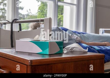 Stilllandschaft: Handschuhe und Gesichtsschutzmaske vor einem Pflegebett Stockfoto