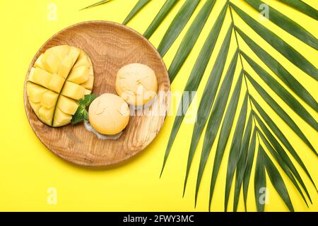Teller mit schmackhaftem Mango-Eis und Palmenblatt Farbiger Hintergrund Stockfoto