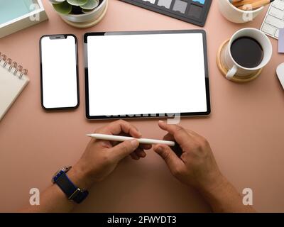 Draufsicht auf Hände von Geschäftsleuten, die den Stift auf dem Arbeitsplatz mit Smartphone, Tablet und Schreibwaren halten, und auf dem Weg zum Beschneiden Stockfoto