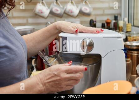 Frau schlägt den Teig mit einem Mixer, um Muffins zuzubereiten Mit getrockneten Tomaten Stockfoto