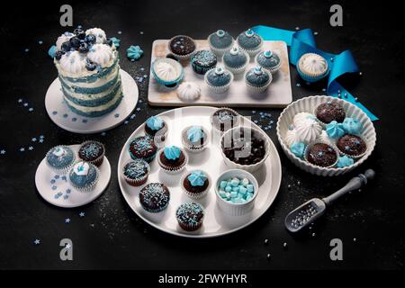 Köstlicher Kuchen und Cupcakes in Blau auf dunklem Hintergrund. Tischkulisse für Feiern. Stockfoto