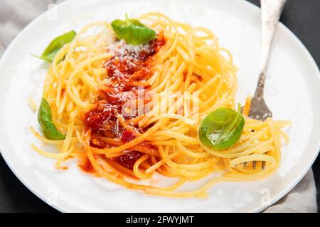 Köstliche, appetitliche italienische Pasta-Spaghetti mit Tomatensauce, Parmesan und Basilikum auf einem Teller auf grauem Hintergrund. Stockfoto