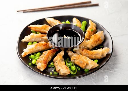 Gebratene Gyoza-Knödel mit Sojasauce und Zwiebel auf hellgrauem Hintergrund. Stockfoto