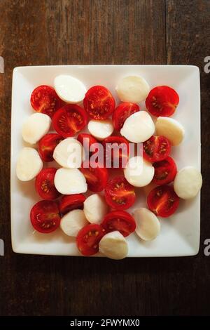 Fein geschnitten in halbfrischen Mini-Mozzarella-Kugeln und Tomaten auf weißem Keramikplatte Stockfoto