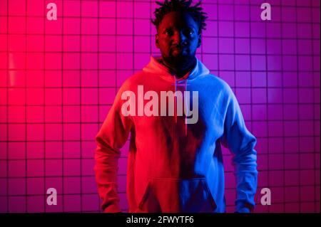 Porträt eines afroamerikanischen Mannes in einem Hoodie auf Neon-Hintergrund. Rot-blauer Hintergrund. Stockfoto