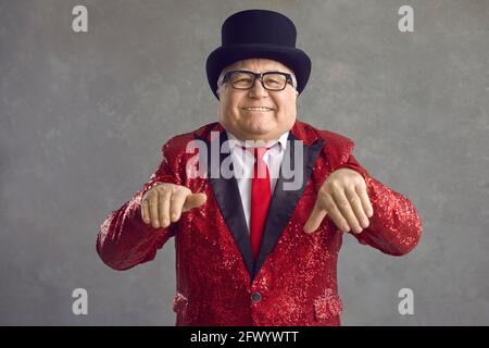 Lustiger molliger reicher älterer Mann in glänzender Jacke und schwarz Hut tanzend und lächelnd Stockfoto