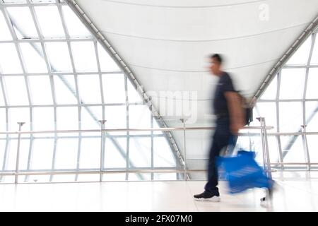 Ein Mann in Bewegungsunschärfe auf weißen Flur mit großen Fenstern. Verschwommene Menschen zu Fuß in einem modernen Gebäude. Abstraktes Bild von Reisenden im lobb Stockfoto