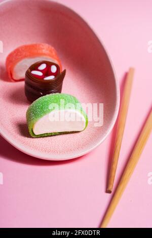 Appetitlich buntes, süßes Sushi auf Keramikplatte mit Holzplatte Essstäbchen auf rosa Hintergrund platziert Stockfoto