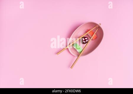 Blick von oben auf appetitlich buntes, süßes Sushi, serviert auf Keramik Teller mit Holzstäbchen auf rosa Hintergrund platziert Stockfoto