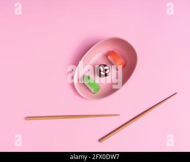 Blick von oben auf appetitlich buntes, süßes Sushi, serviert auf Keramik Teller mit Holzstäbchen auf rosa Hintergrund platziert Stockfoto