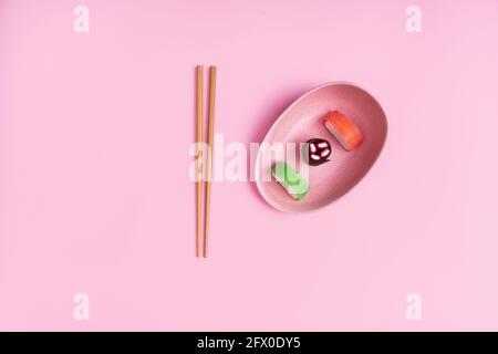Blick von oben auf appetitlich buntes, süßes Sushi, serviert auf Keramik Teller mit Holzstäbchen auf rosa Hintergrund platziert Stockfoto